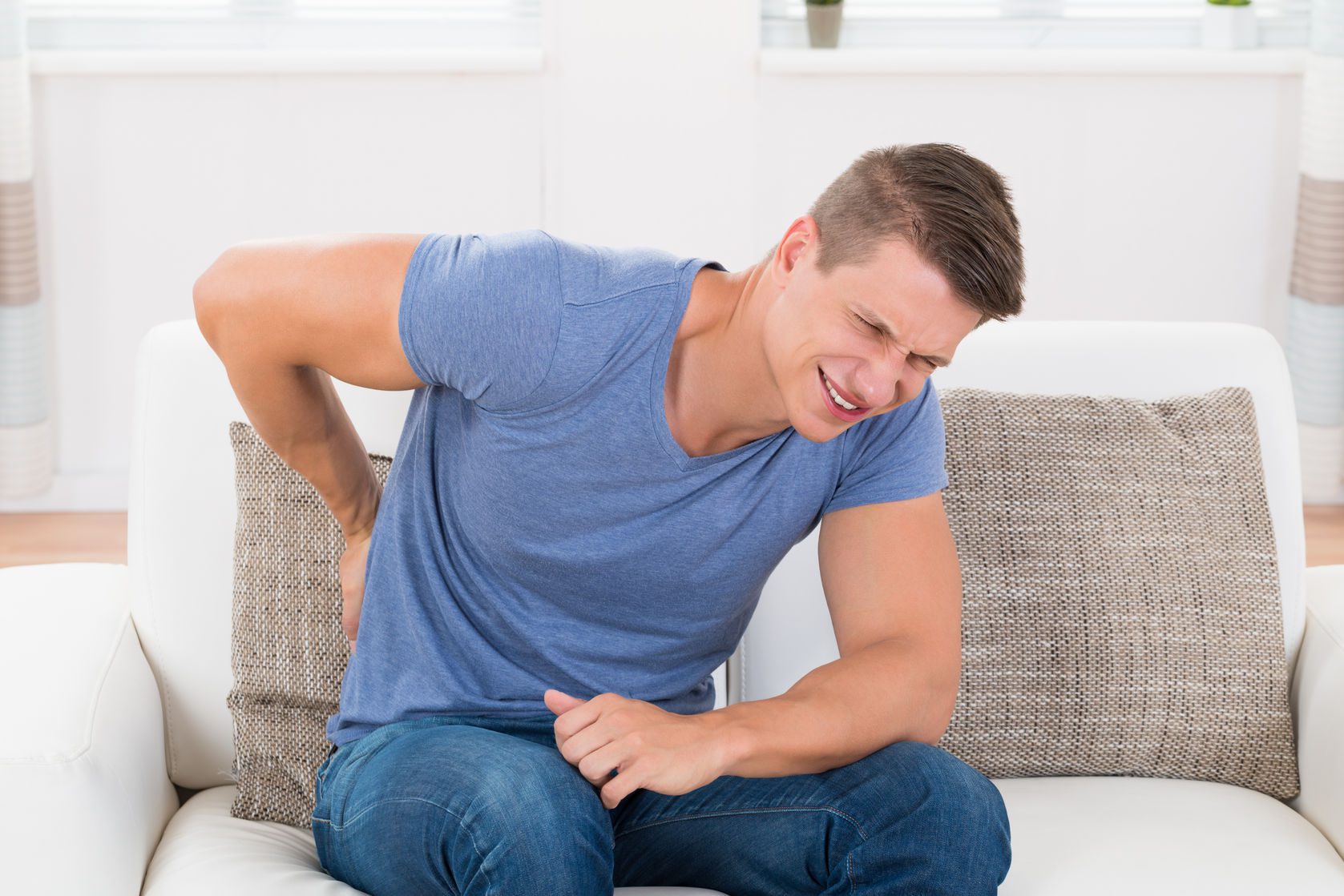 young man on sofa suffering from backpain at home